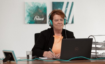 Beispielbild OnlineCoaching: Eine Frau mit Headset und Stift in der Hand vor ihrem Laptop.