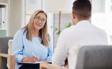 Beispielfoto Beratungssituation: Zwei Personen sitzen sich im Gespräch in einem modernen Büro gegenüber.