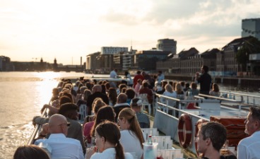 Foto: Blick auf die feiernde Gesellschaft an Bord bei untergehender Sonne.